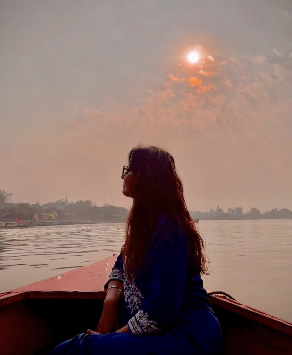 Shatakshi on a boat at dusk, sun low over the water